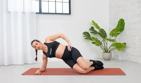 Donna in posizione di plank laterale, con un movimento di circonduzione del busto per rafforzare gli obliqui.