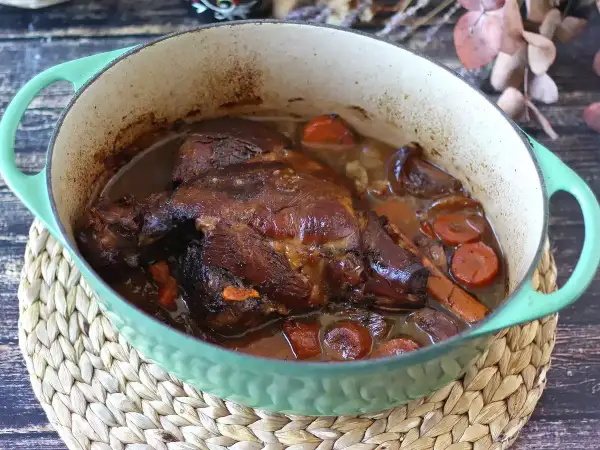 Un gigot de 7 heures mijoté dans une cocotte verte, avec des carottes et des oignons. La viande est tendre et dorée, prête à être dégustée.