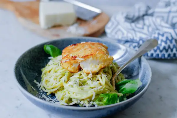 Pyszny makaron z rybą w panierce, posypany parmezanem i udekorowany bazylią. Danie wygląda apetycznie i zachęca do spróbowania.