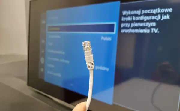 Kabel sieciowy Ethernet zbliżenie na wtyczkę RJ45 na tle ekranu telewizora z menu ustawień.