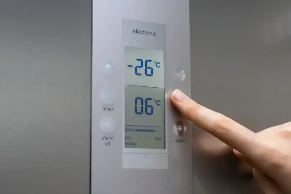 Palec naciska przycisk plus na panelu sterowania lodówki, regulując temperaturę. Na wyświetlaczu widać -26°C i 06°C.