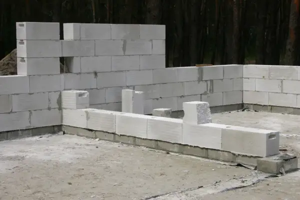Budowa domu z betonu komórkowego. Ściany wznoszone z białych bloczków, w tle las.