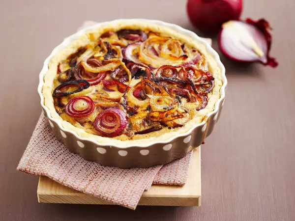 Tarte à l'oignon dorée et appétissante, garnie d'oignons caramélisés et d'une pâte croustillante. Un délice visuel et gustatif.