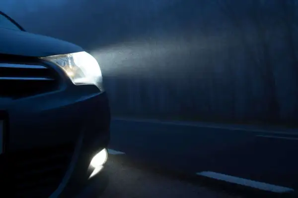 Las luces de posición de un coche iluminan la niebla en una carretera oscura, revelando el camino y los árboles a los lados.