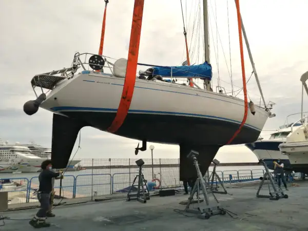 Barca a vela sollevata da gru, pronta per la manutenzione dello scafo e l'applicazione dell'antivegetativo.