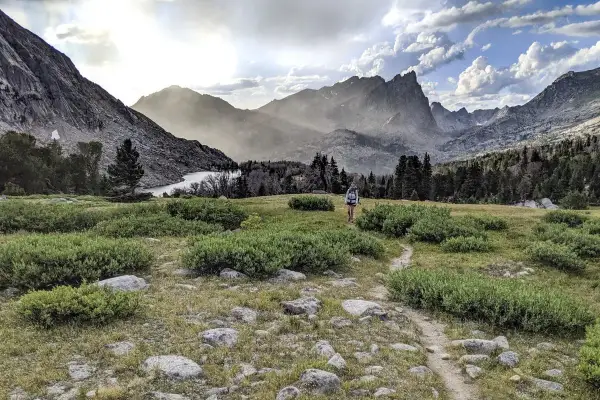 Wanderer auf dem Continental Divide Trail wandern durch eine bergige Landschaft mit einem See und bewaldeten Hängen.