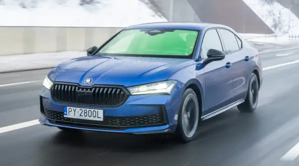 Niebieska Skoda Superb 2.0 TSI pędzi po mokrej drodze, tworząc wrażenie prędkości.