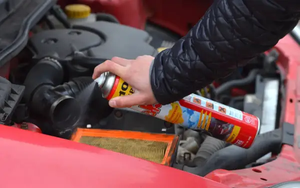 Ręka trzyma puszkę z preparatem do rozruchu silnika, rozpylając go w okolicy filtra powietrza. Czy odpalanie na plaka jest szkodliwe?