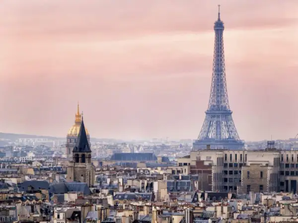 Eiffeltornet höjd över Paris takåsar i rosa skymningsljus. En gyllene kupol syns i bakgrunden.