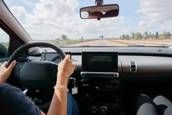 Vue du **rétro intérieur position nuit** d'une voiture. Mains sur le volant, route dégagée sous un ciel nuageux.