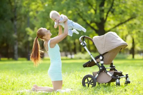 Mama podrzuca noworodka w wózku na trawie w parku.