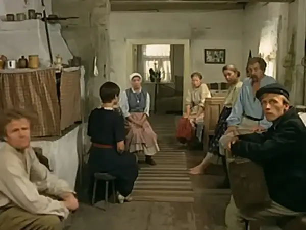 Scena z filmu "Znachor", gdzie nagrywali w wiejskiej chacie. Ludzie siedzą w skromnym wnętrzu, czekając na pomoc.