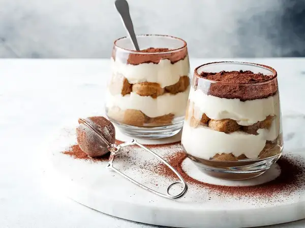 Dwa pucharki z deserem tiramisu, warstwy biszkoptów i kremu, posypane kakao. Idealna mizeria na słodko.