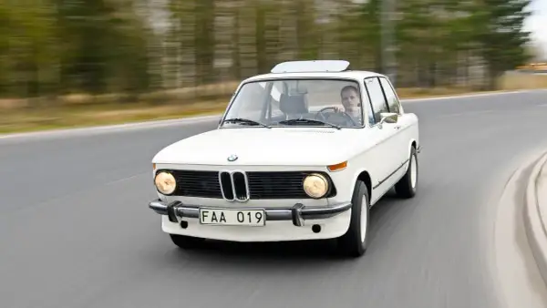 Vit BMW 70-talsklassiker kör på en väg, med en man bakom ratten.