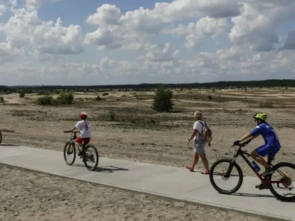 Ludzie na rowerach i pieszo na ścieżce rowerowej w krajobrazie pustynnym.