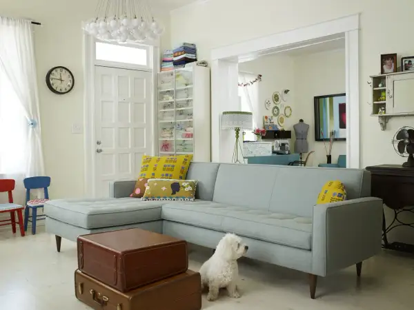 Un salotto accogliente con divano azzurro, cuscini decorati e un cane bianco. L'ambiente è dominato da **colori pastello** e dettagli vintage.
