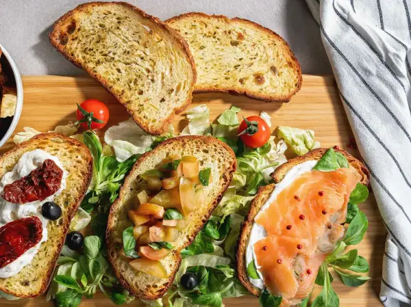 Bruschette senza pomodoro: fette di pane tostato con salmone, crema, pomodori secchi e verdure fresche.