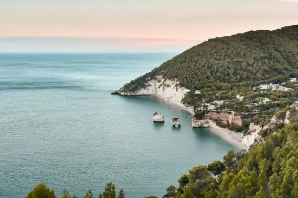 Baia con scogliere bianche e mare azzurro, perfetta per una passeggiata dell'amore. Alberi verdi e case bianche punteggiano la costa.