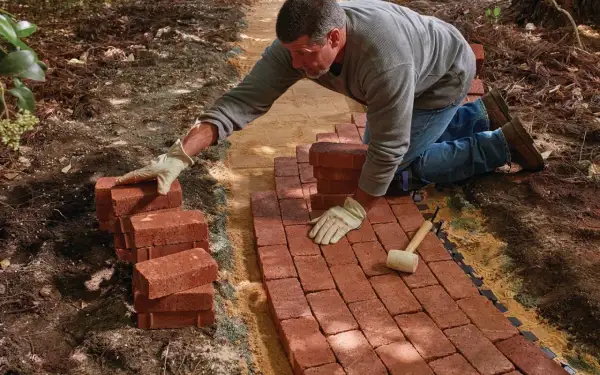 Man laying red bricks to create a new brick walkway in a garden.
