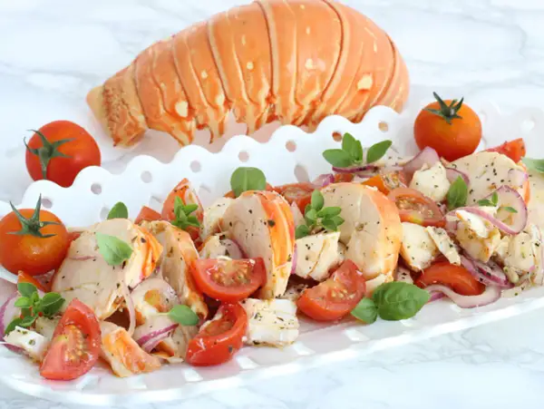 Aragosta alla catalana, un piatto fresco con code di aragosta, pomodorini, cipolla rossa e basilico, guarnito con una coda intera.