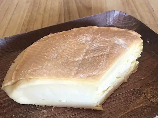 Un morceau de fromage à pâte molle, à la croûte orangée et à l'odeur prononcée, servi sur un plateau en bois.