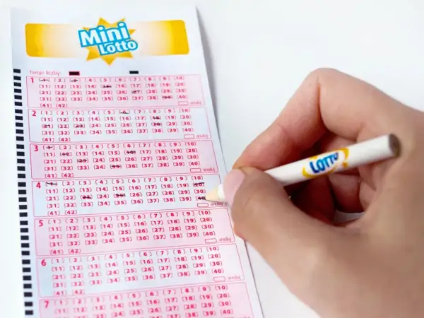 Ręka zaznacza liczby na kuponie Mini Lotto. To kaskada zasady, gdzie każda kolejna linijka to szansa na wygraną.