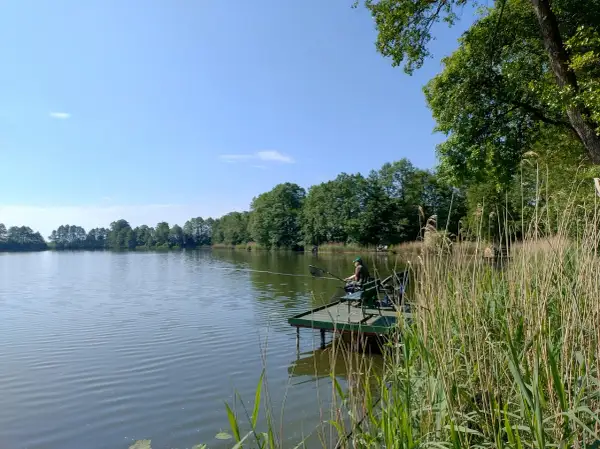 Wędkarz na pomoście nad spokojnym zalewem w Nowym Mieście. Otoczenie zieleni i błękitne niebo tworzą sielski krajobraz.