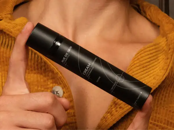 Dłoń trzyma czarny flakon kremu z napisem "Niacynamid". Czy wybrać retinol czy niacynamid?