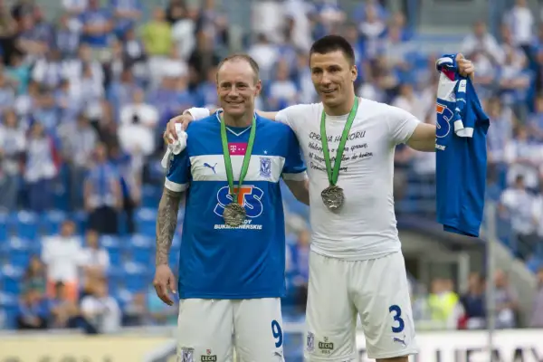 Dwóch piłkarzy z medalami na szyi, jeden z koszulką w ręku. Uśmiechnięci, świętują sukces, być może to koniec kariery.