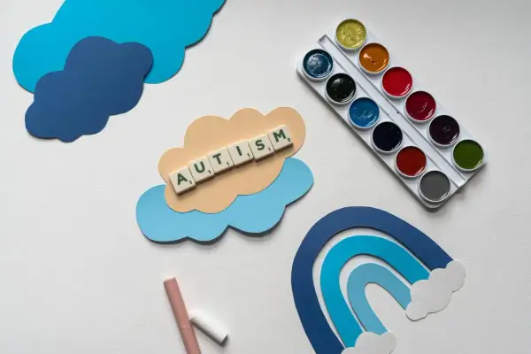Terapia dziecka z aspergerem w domu: chmurki, tęcza, kredki i farby. Słowo AUTISM ułożone z liter.
