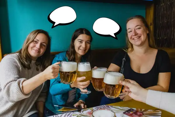 Trzy uśmiechnięte kobiety wznoszą kufle piwa. Jedna z nich mówi "Dzień dobry po czesku!".