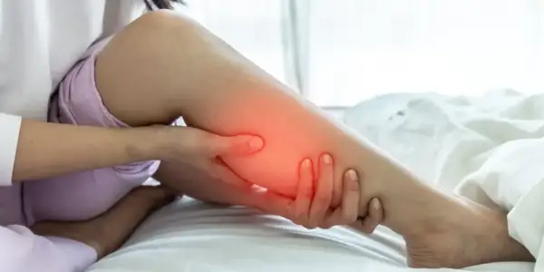 Une personne se tient la jambe, une zone rouge vif sur le mollet indiquant une douleur.