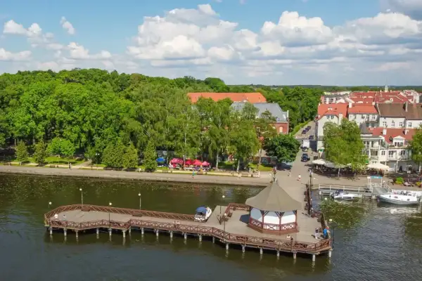 Drewniane molo z altaną i łodziami, nad jeziorem w otoczeniu zieleni i urokliwego miasteczka. Idealne mazury atrakcje dla każdego.