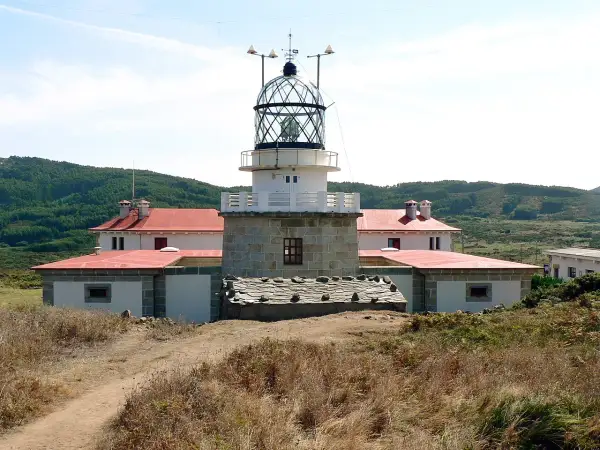 El faro de estaca de bares se alza imponente sobre la costa, con sus edificios blancos y tejados rojos rodeados de vegetación.