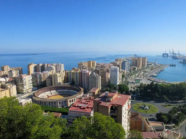 Vista panorámica desde el mirador de Gibralfaro: la plaza de toros, el puerto y la ciudad de Málaga bajo un cielo azul.
