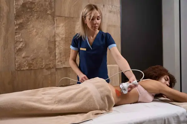 Terapista esegue crioterapia fisioterapia su paziente sdraiata, usando un manipolo con luce rossa sulla schiena.
