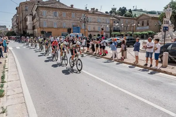Ciclisti in gara durante il Giro d'Italia Marche, acclamati da spettatori festanti lungo la strada.