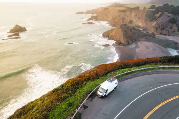 Biały kamper na krętej drodze wzdłuż wybrzeża Pacyfiku, idealny na road trip USA. Fale rozbijają się o skaliste klify.