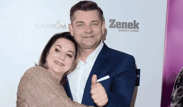 Danuta Martyniuk, w złotej sukience, przytula się do mężczyzny w granatowym garniturze, który pokazuje kciuk w górę.