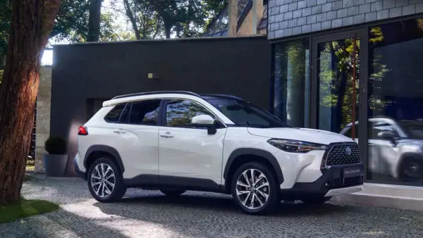 Biała Toyota Corolla Cross zaparkowana przed nowoczesnym budynkiem. Poznaj jej wymiary i możliwości.
