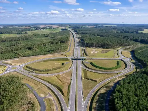 Nowa droga ekspresowa, idealna trasa do Kołobrzegu, przecina lasy i pola. W oddali widać farmę wiatrową.
