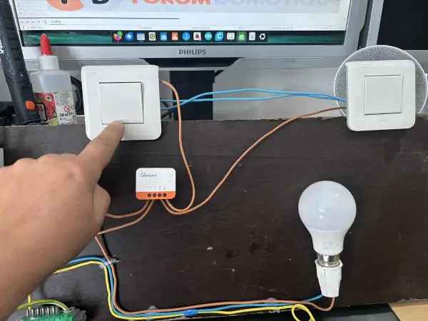 Installation d'un interrupteur zigbee va et vient. Un doigt actionne un interrupteur connecté à un module Sonoff, pilotant une ampoule.