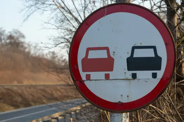 Znak drogowy informujący o końcu zakazu wyprzedzania. Dwa samochody, czerwony i czarny, symbolizują koniec ograniczenia.