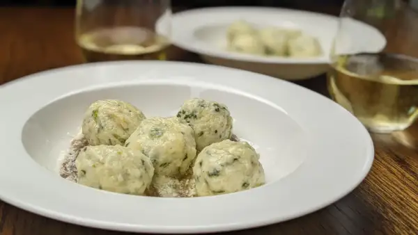 En tallrik med fluffiga gnudi, perfekt för ett enkelt gnudi recept. Serveras med riven ost och ett glas vitt vin.