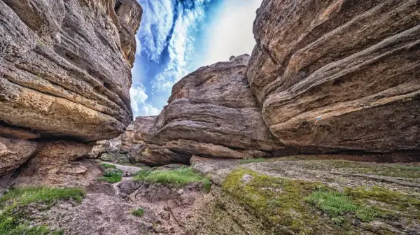 Sendero entre imponentes rocas erosionadas, con el cielo azul y nubes blancas asomando. Un paisaje que evoca la grandeza de los Picos de Urbión.