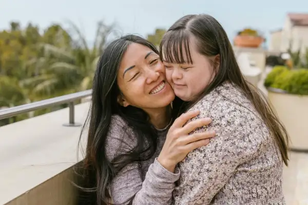 Abbraccio affettuoso tra due donne, una con sindrome di Down, che condividono un momento di gioia e amore.