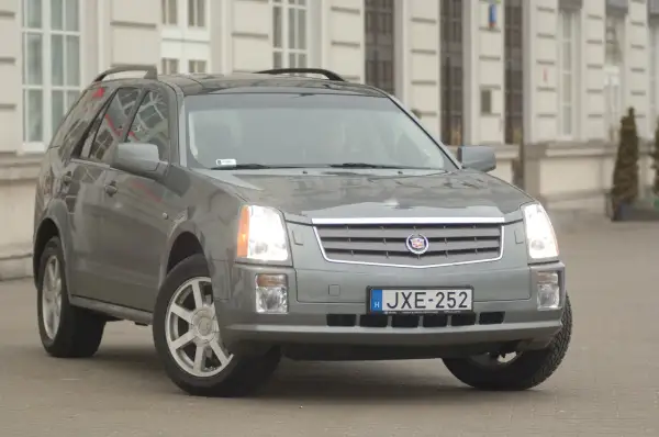 Szary Cadillac SRX z tablicą rejestracyjną JXE-252 zaparkowany przed budynkiem.