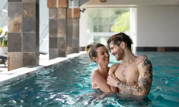 Para w basenie SPA, uśmiechnięci, patrzą na siebie.