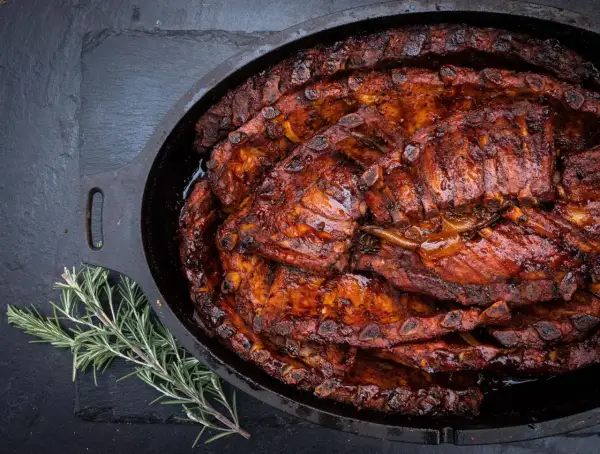 Saftige spareribs im Dutch Oven, glasiert und bereit zum Genießen. Ein Rosmarinzweig liegt daneben.
