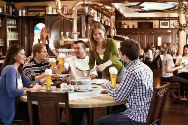 Gäste genießen Bier und Essen im Erdinger Brauhaus. Eine Kellnerin serviert, während Freunde lachen und trinken.